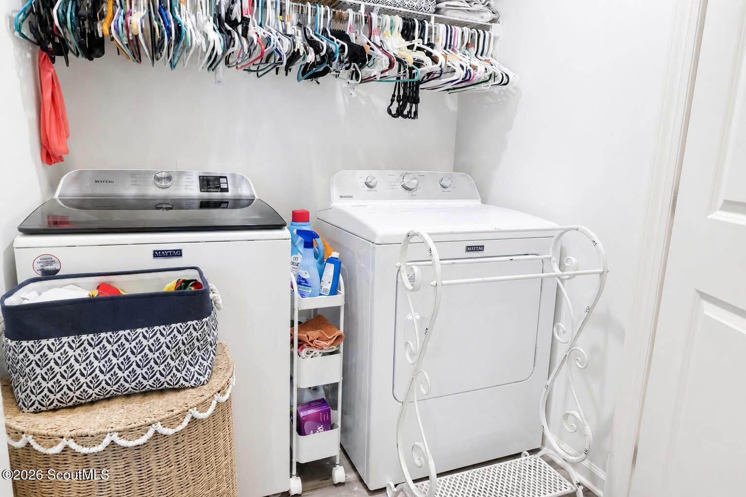 Laundry room with Maytag washer and dryer beneath a clothes rod, with woven baskets and a rolling storage cart.