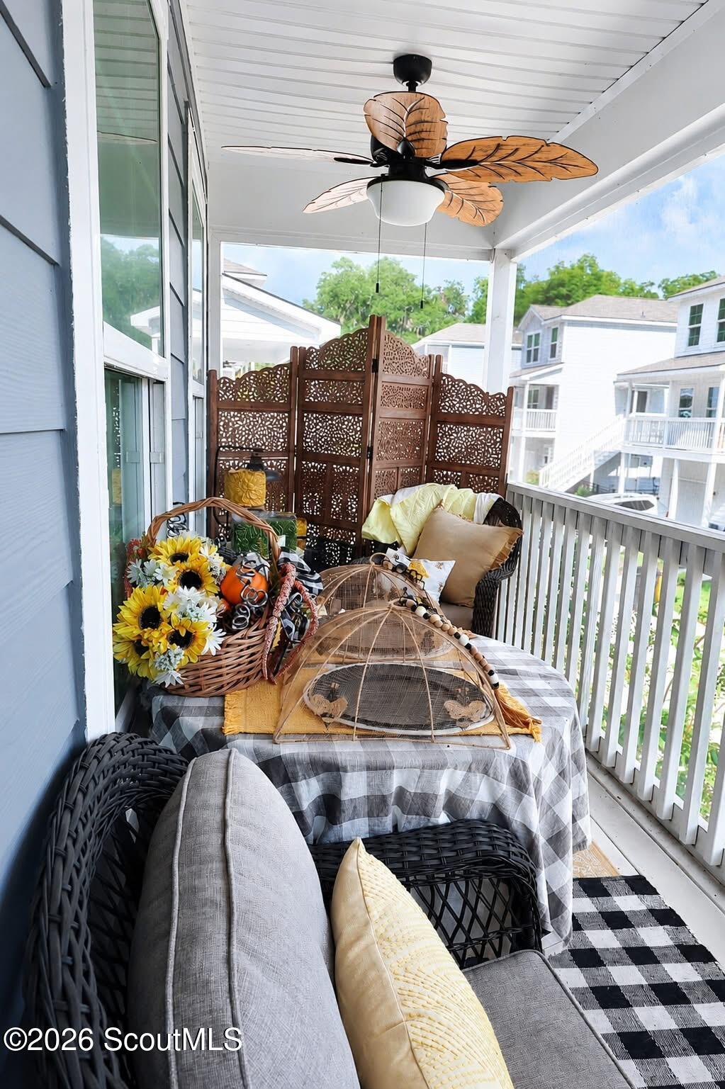 Furnished covered porch with wicker seating, floral decorations, and a leaf-blade ceiling fan.