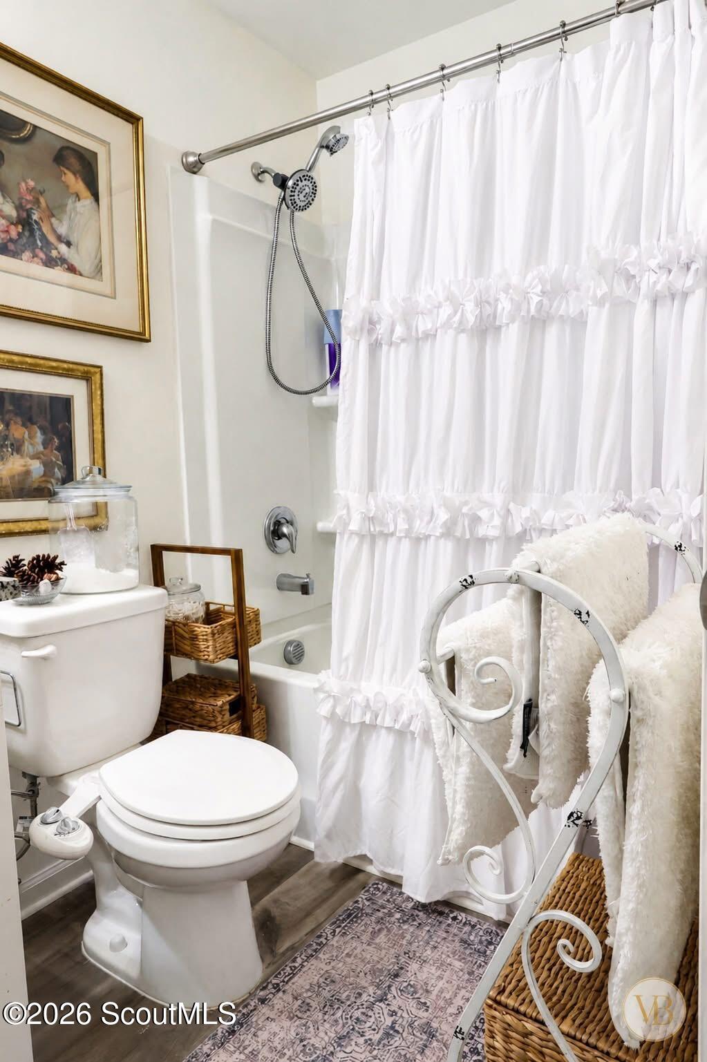 Bathroom with a ruffled white shower curtain, handheld showerhead and decorative towel rack.