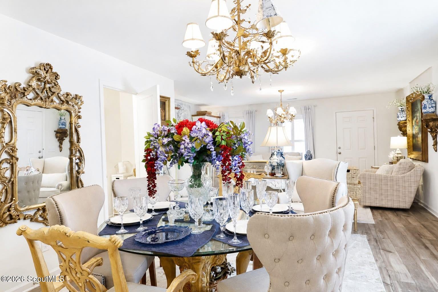 Furnished dining room with a set table, colorful floral centerpiece, and ornate gold chandeliers.