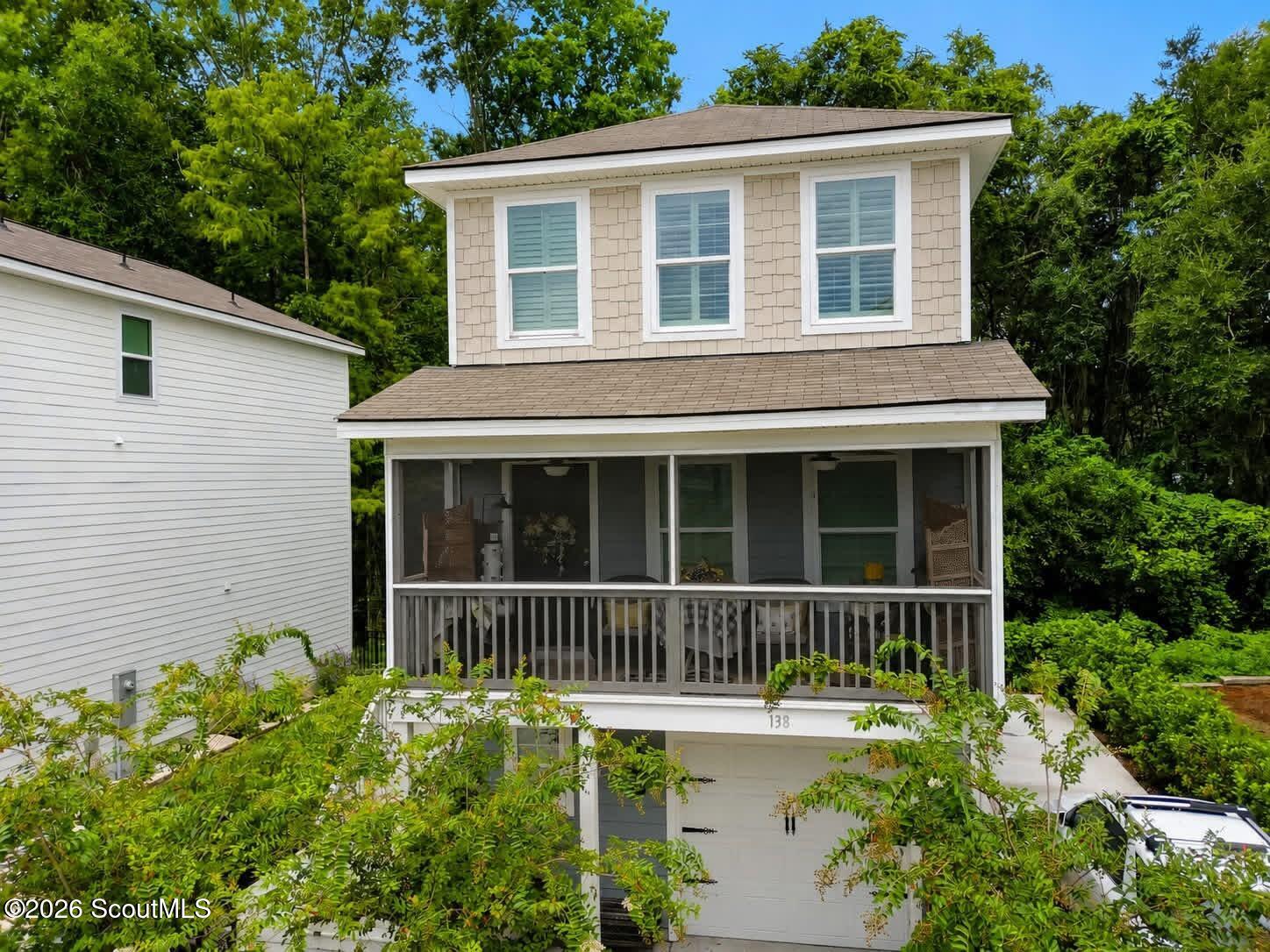 Two-story shingle-sided home with a screened porch above a garage, framed by trees.