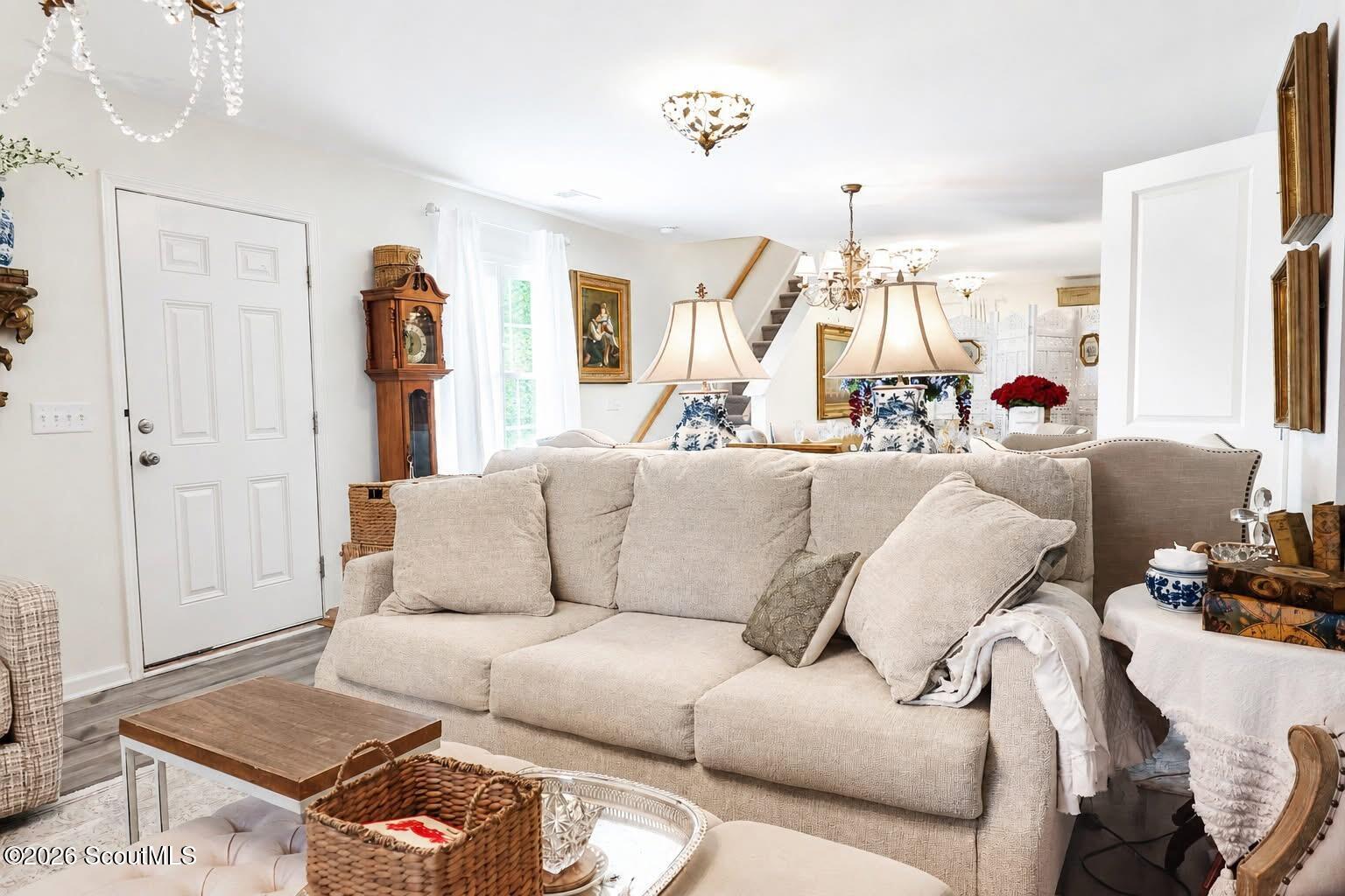 Furnished living room with a cream sectional, grandfather clock, and staircase.