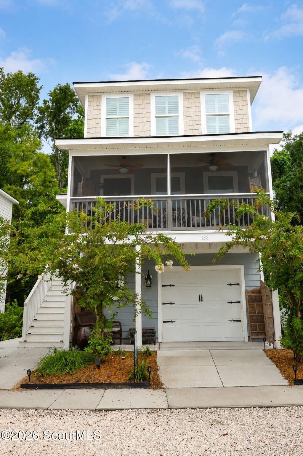 Raised home with a screened porch, white garage door, exterior stairs, and leafy landscaping.