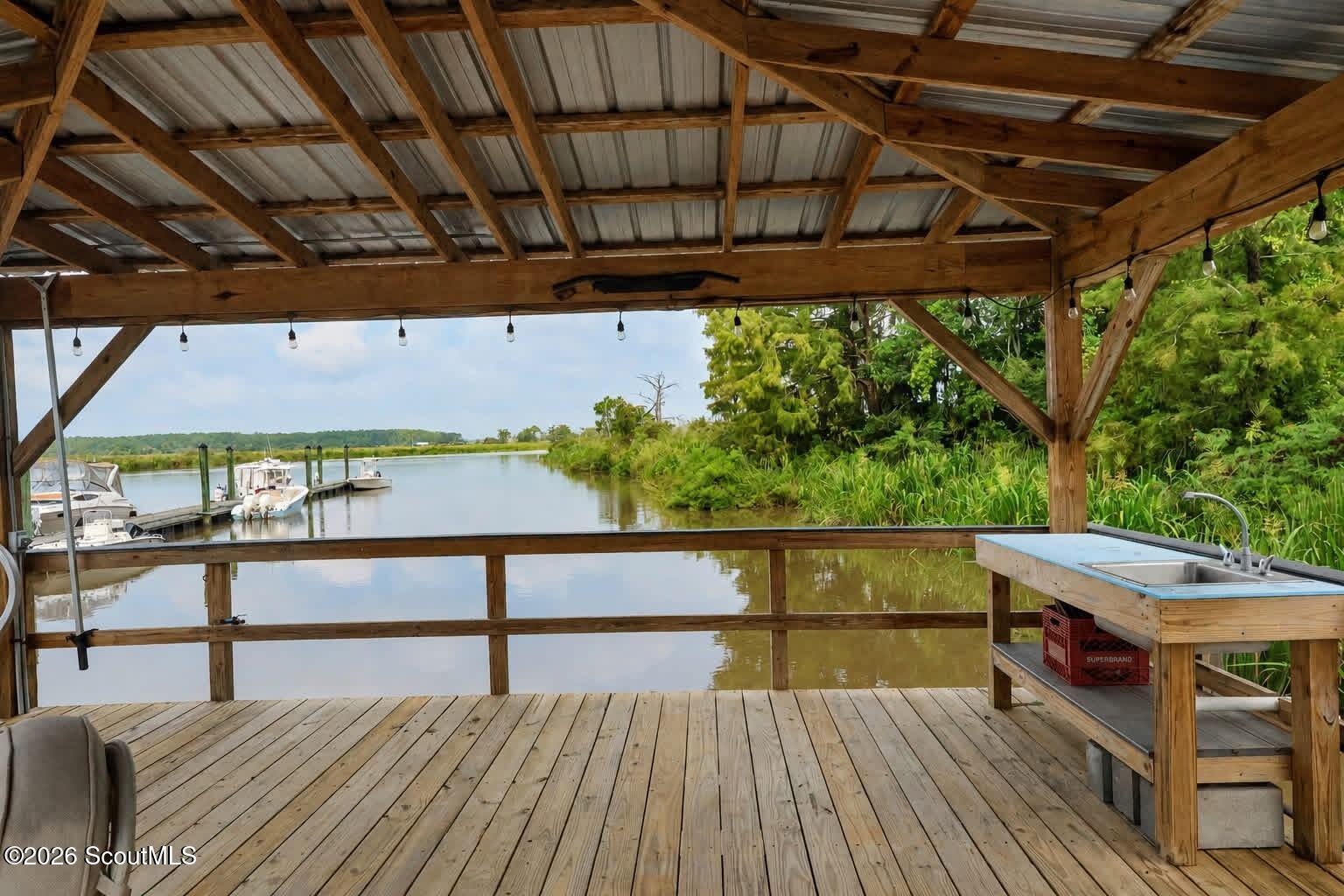 Covered wooden dock with a built-in sink overlooking moored boats and a calm, green-lined waterway.
