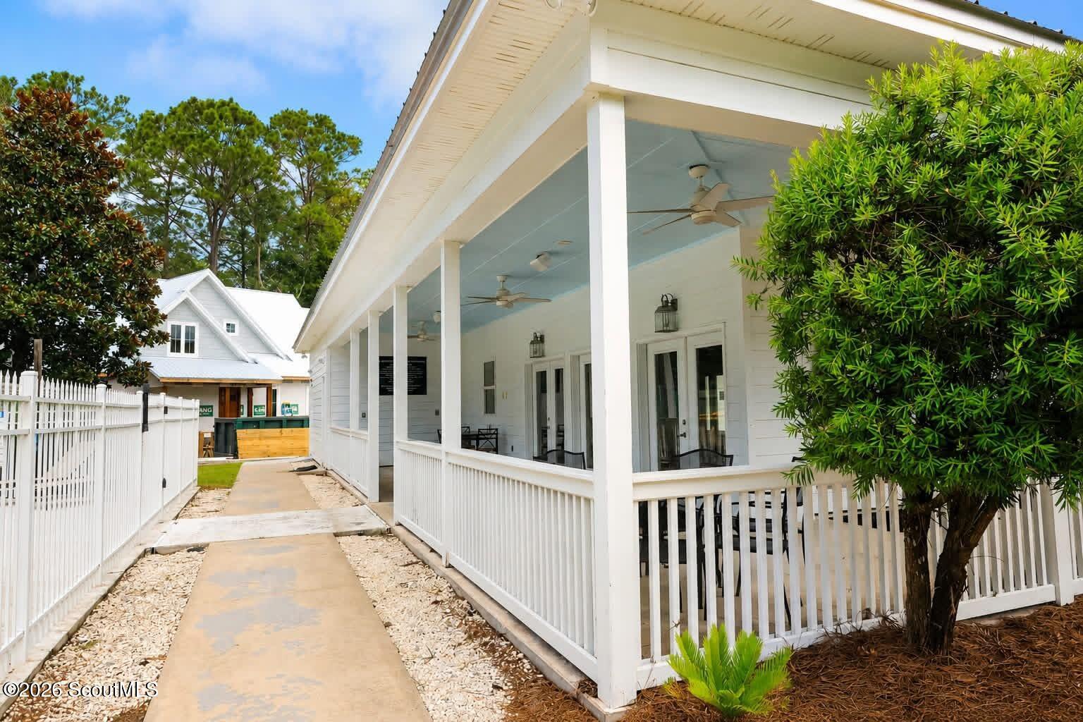 White home with a long covered porch, ceiling fans, and a walkway bordered by white fencing.