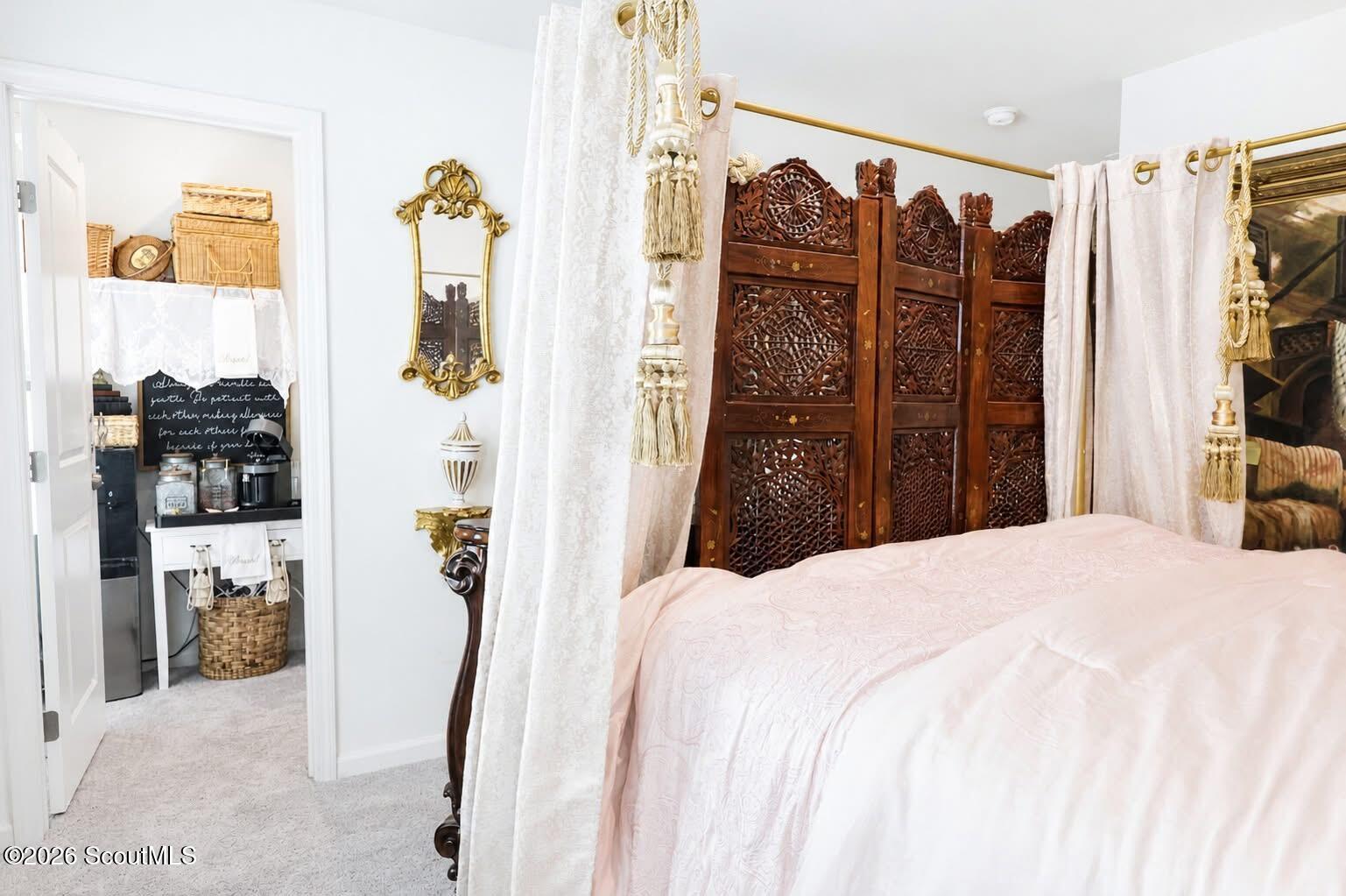 Bedroom with a pale pink bedspread, carved wooden screen, and sheer curtains.