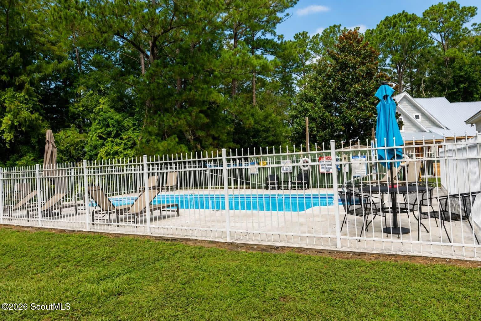 Fenced outdoor swimming pool with lounge chairs and a patio dining set.