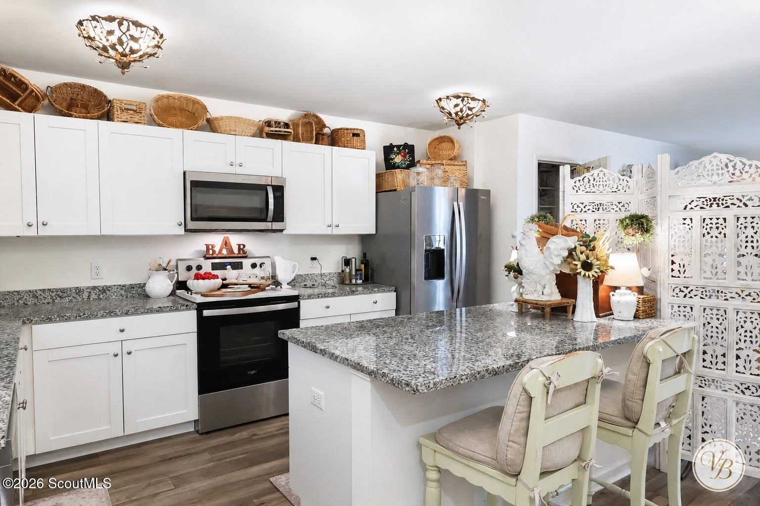 Kitchen with white cabinets, stainless appliances, a granite island, and wicker baskets above the cabinets.