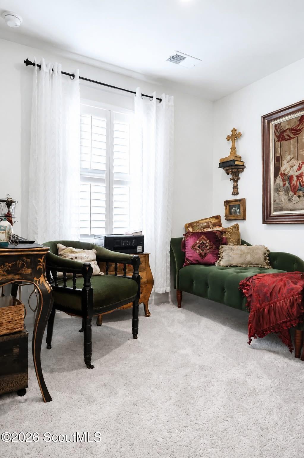 Furnished sitting room with green sofas, white shuttered window, and ornate wooden furniture.