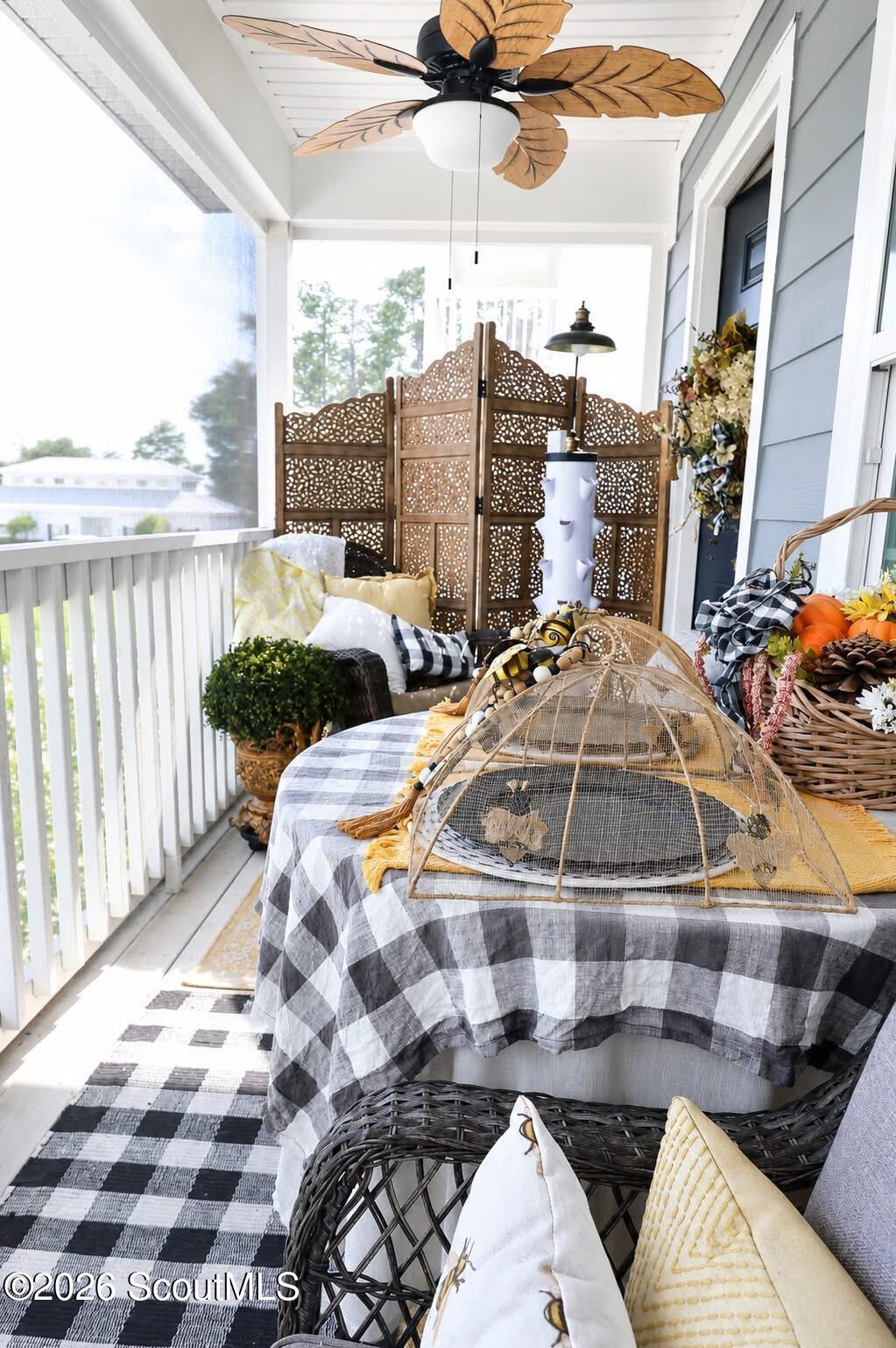 Screened porch with wicker seating, a checkered table, and a leaf-shaped ceiling fan.