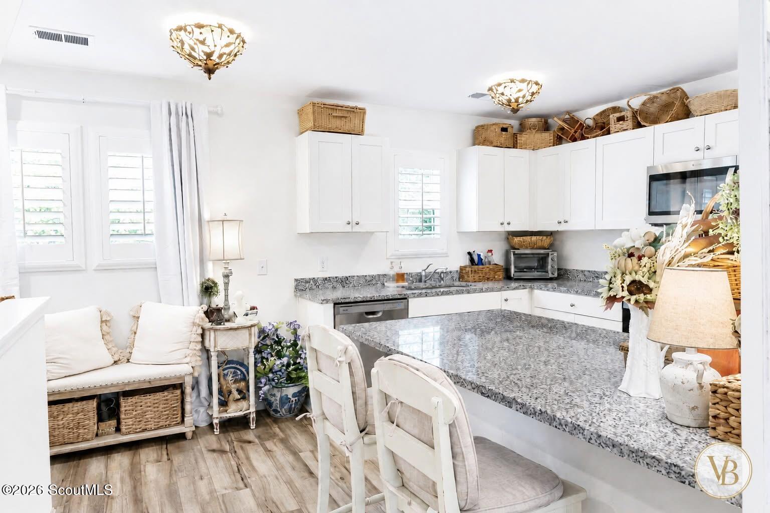 Bright white kitchen with gray patterned countertops, a breakfast bar, and white chairs.