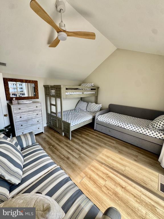 Bedroom with a wooden bunk bed, gray daybed, striped sofa, and ceiling fan.