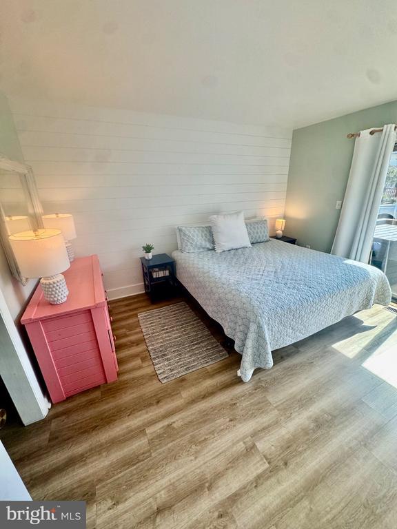 Bedroom with a large bed, pink dresser, white shiplap wall, and wood-look flooring.