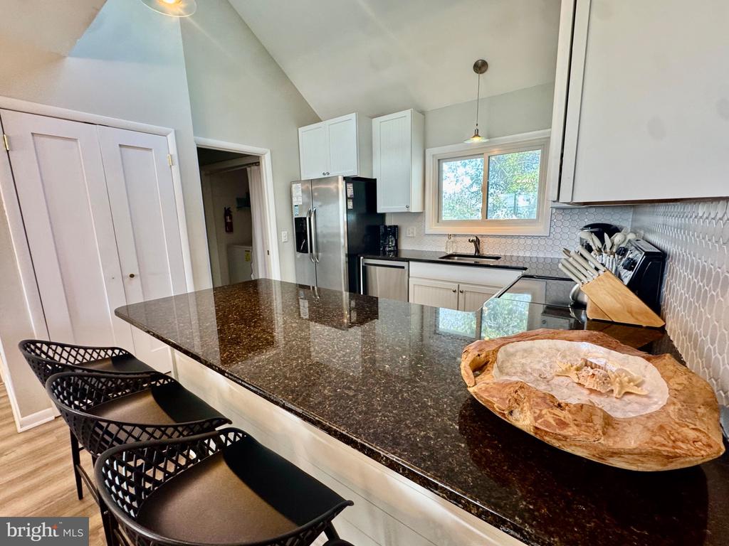 Kitchen with a large dark granite island, black bar stools, white cabinets, and a window above the sink.