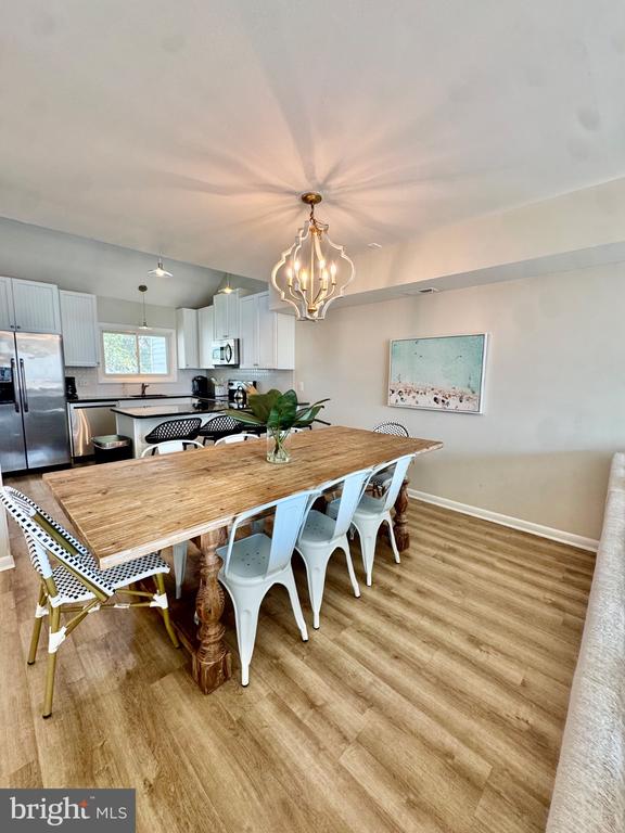 Dining area with a rustic wood table, white chairs, and an open kitchen.