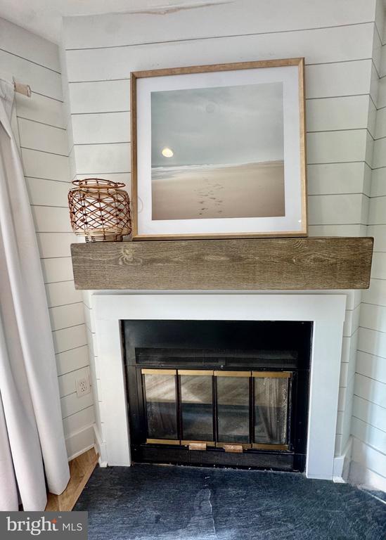 Fireplace with a rustic wood mantel, black insert, slate hearth, and framed beach artwork.