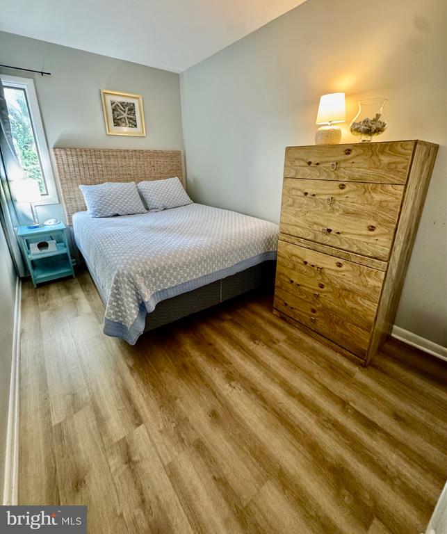 Bedroom with a woven-headboard bed, tall wooden dresser, and wood-look flooring.