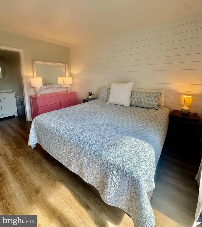 Furnished bedroom with a large patterned bed, pink dresser, and open bathroom doorway.