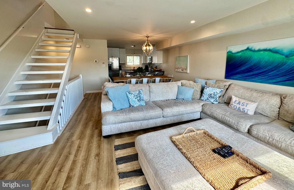Open-plan living room with a large sectional, white staircase, and kitchen dining area beyond.