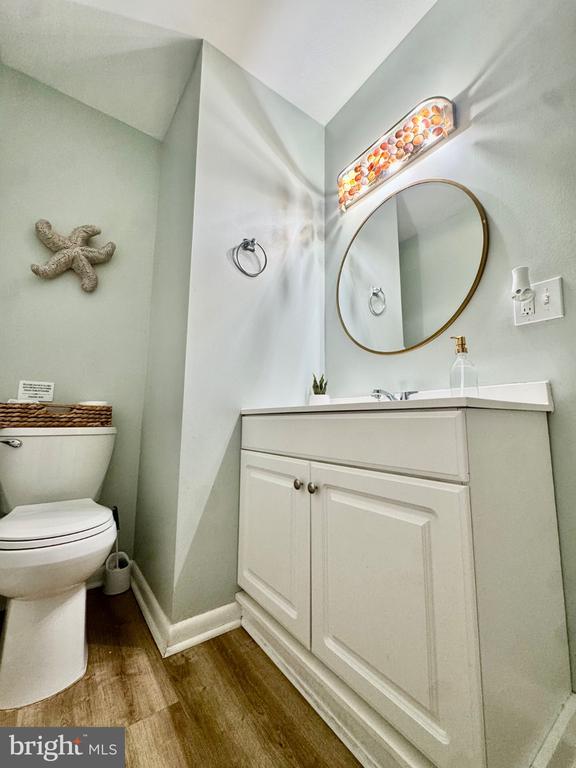 Bathroom with a white vanity, oval mirror, toilet, and colorful light fixture.