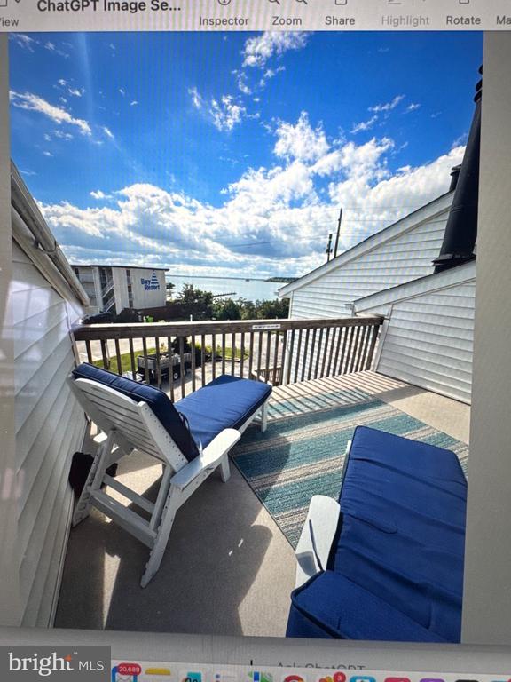 Rooftop deck with blue lounge chairs, a striped rug, and water visible beyond the railing.