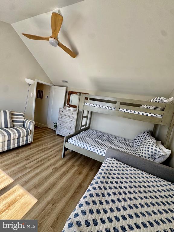 Bedroom with a wooden bunk bed, patterned bedding, striped armchair, and ceiling fan.