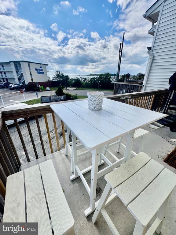 Deck with white outdoor dining set overlooking a resort and distant water.