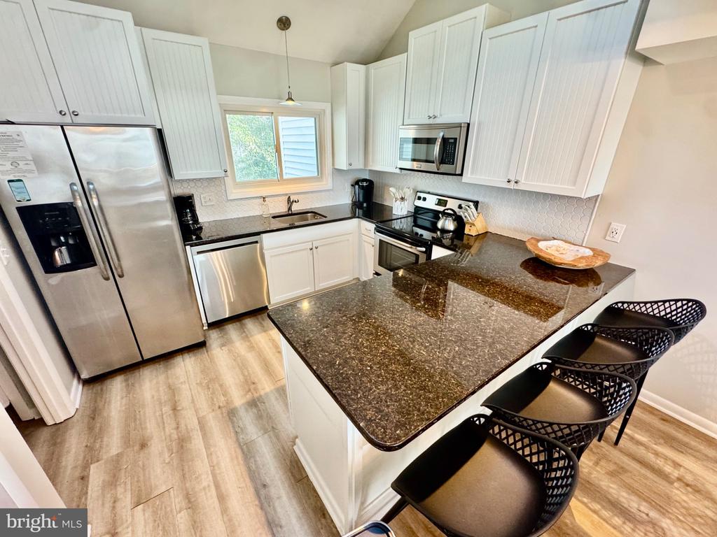 Modern kitchen with stainless steel appliances, dark granite island, and black bar stools.