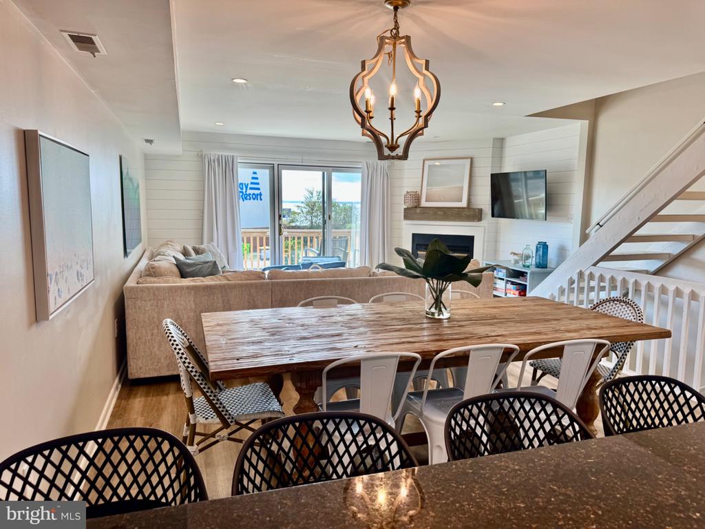 Open-plan living and dining area with a rustic wood table, fireplace, and balcony water view.