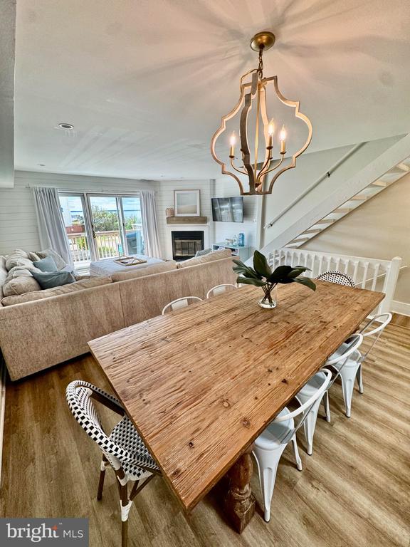 Open-plan dining and living area with a rustic wood table, fireplace, and staircase.