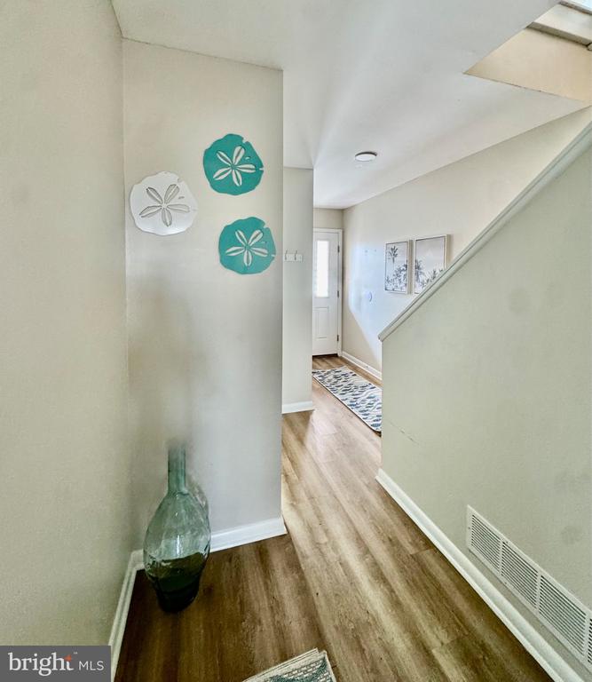 Hallway with wood-look flooring, a staircase, and sand dollar decorations near the entry door.