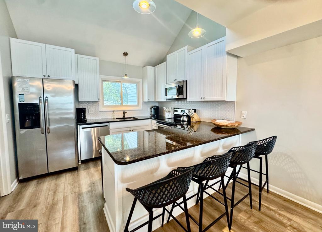 Kitchen with white cabinets, stainless steel appliances, and a granite island with black bar stools.
