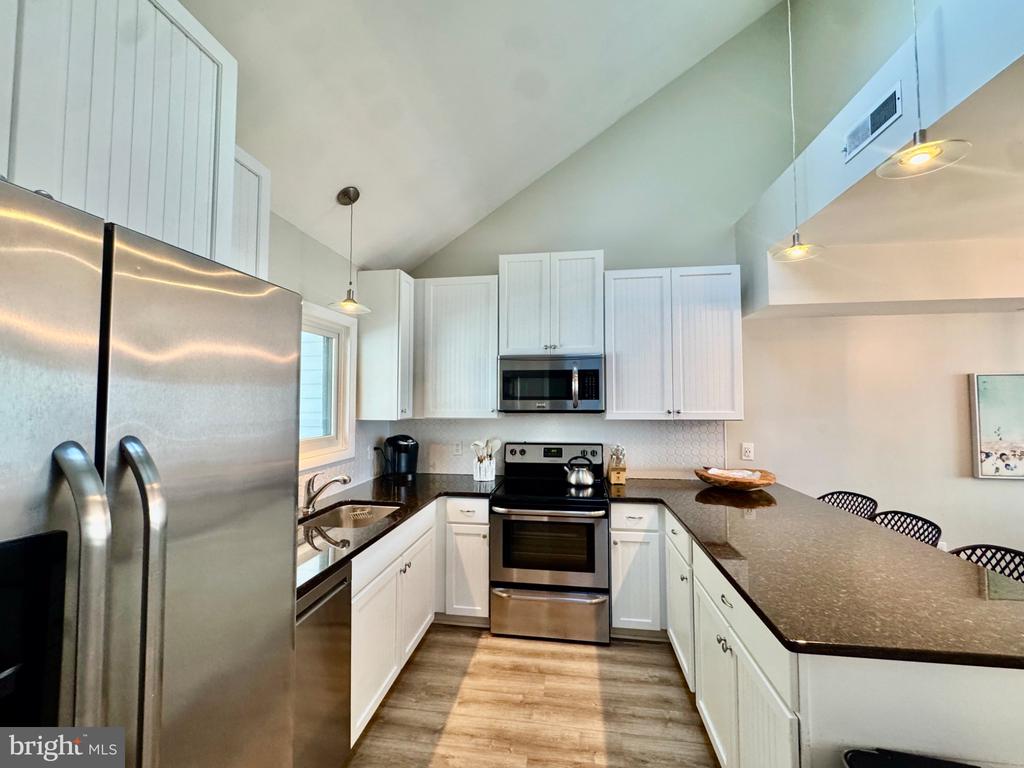 Kitchen with white cabinets, stainless steel appliances, and a long peninsula beneath a vaulted ceiling.