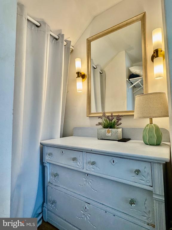 Bathroom vanity with a pale blue dresser, gold-framed mirror, and shower curtain.