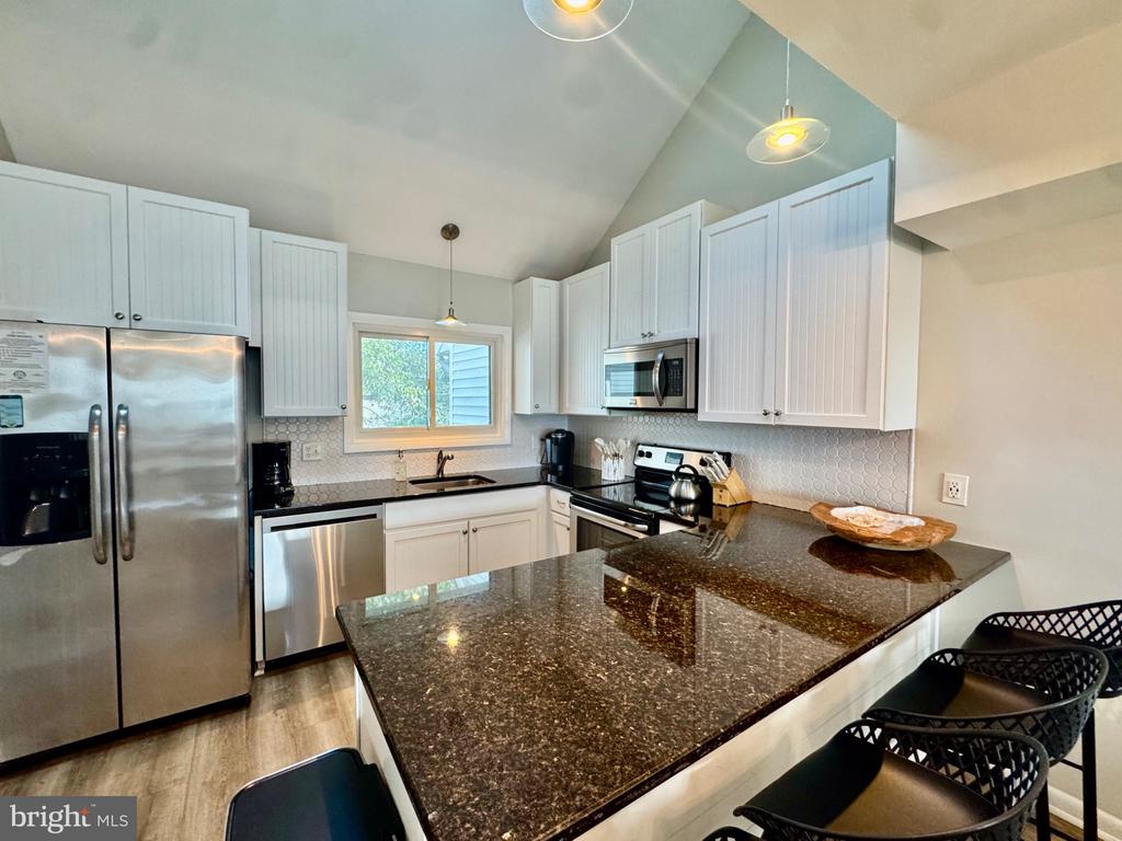 Kitchen with white cabinets, stainless steel appliances, and a large granite island with bar seating.