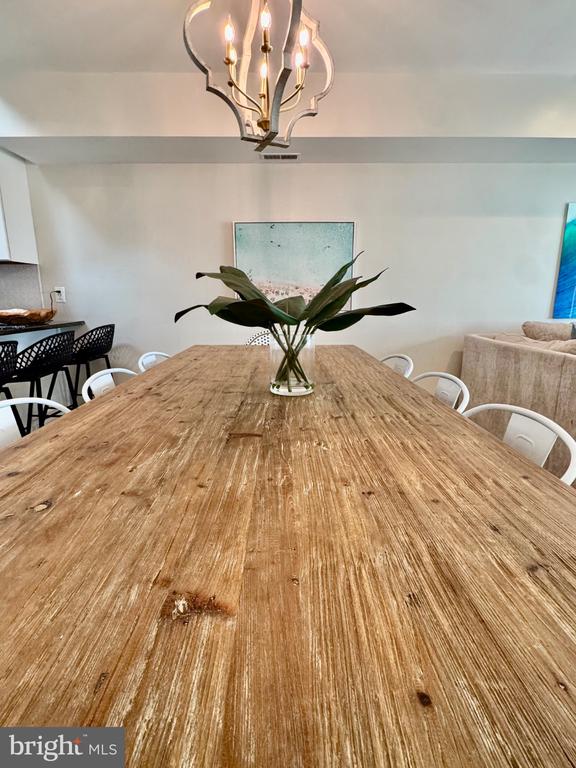 Dining area with a long rustic wood table, white chairs, and a sculptural chandelier.
