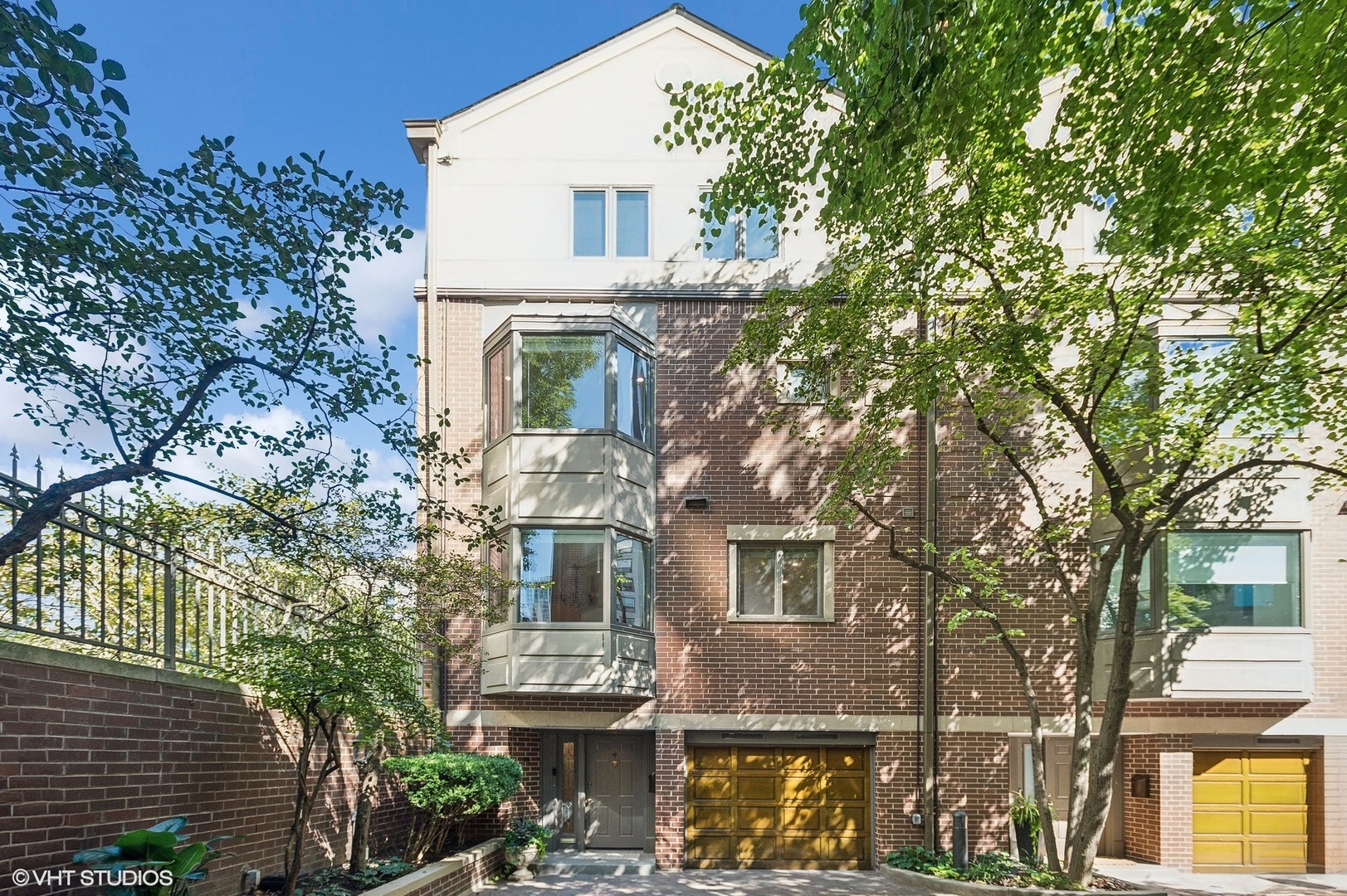 Brick townhouse exterior with projecting bay windows and a garage, framed by leafy trees.