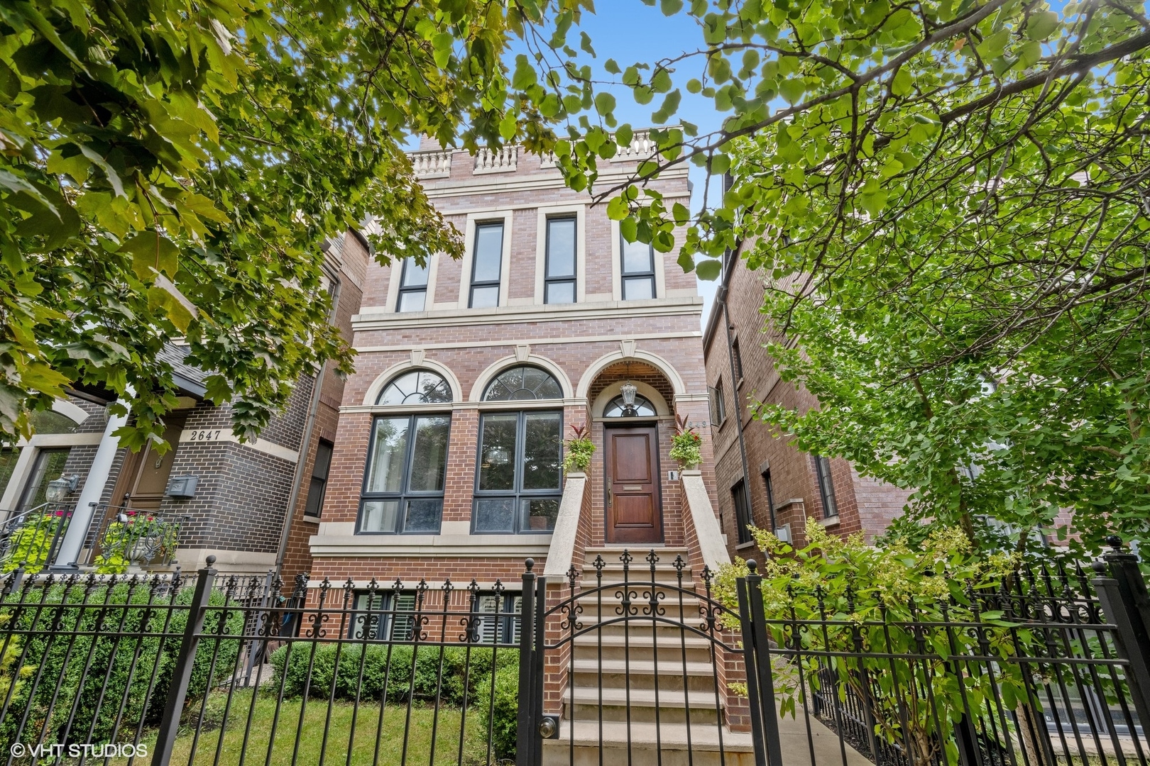 Red-brick Chicago home with arched windows, a raised entrance, and an ornate iron fence.