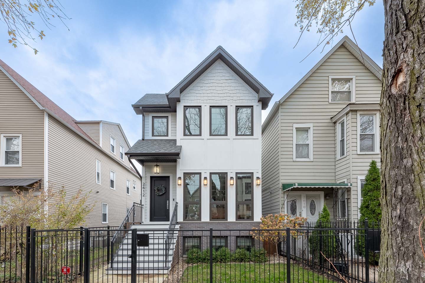 Modern two-story white house with a steep gable, dark-framed windows, and a black iron front fence.