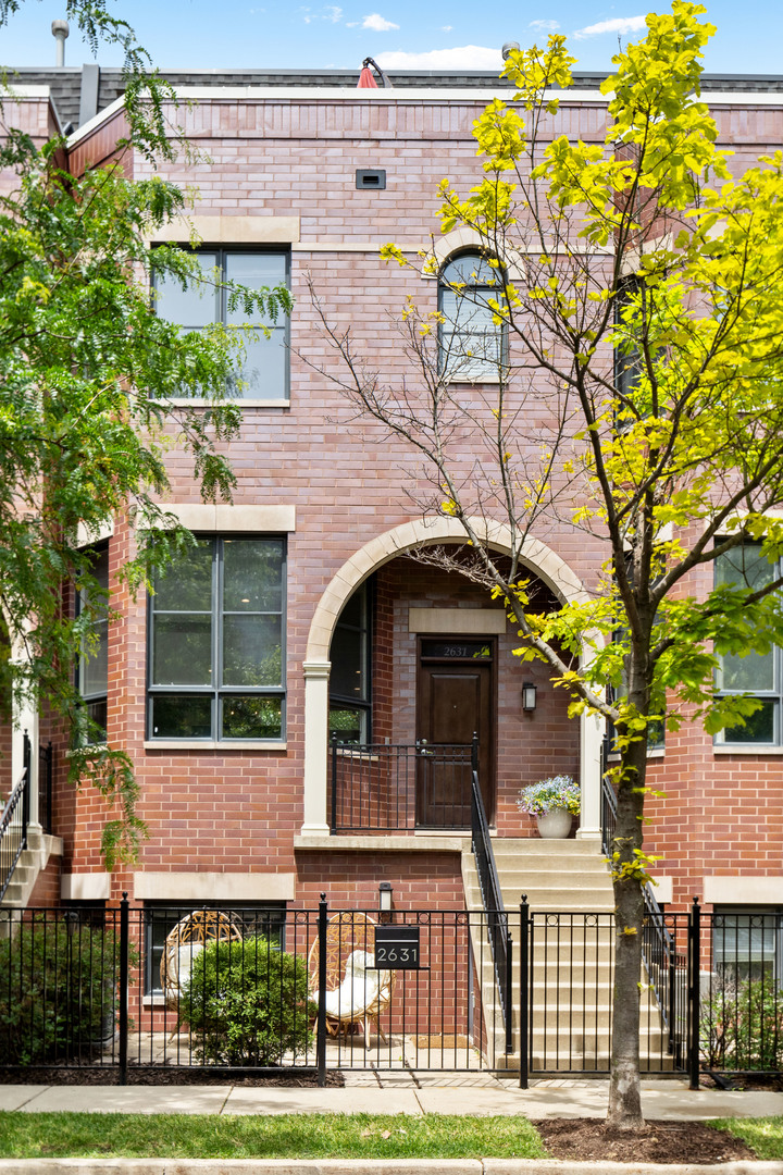 Red brick townhouse with an arched entry, front steps, and leafy trees.