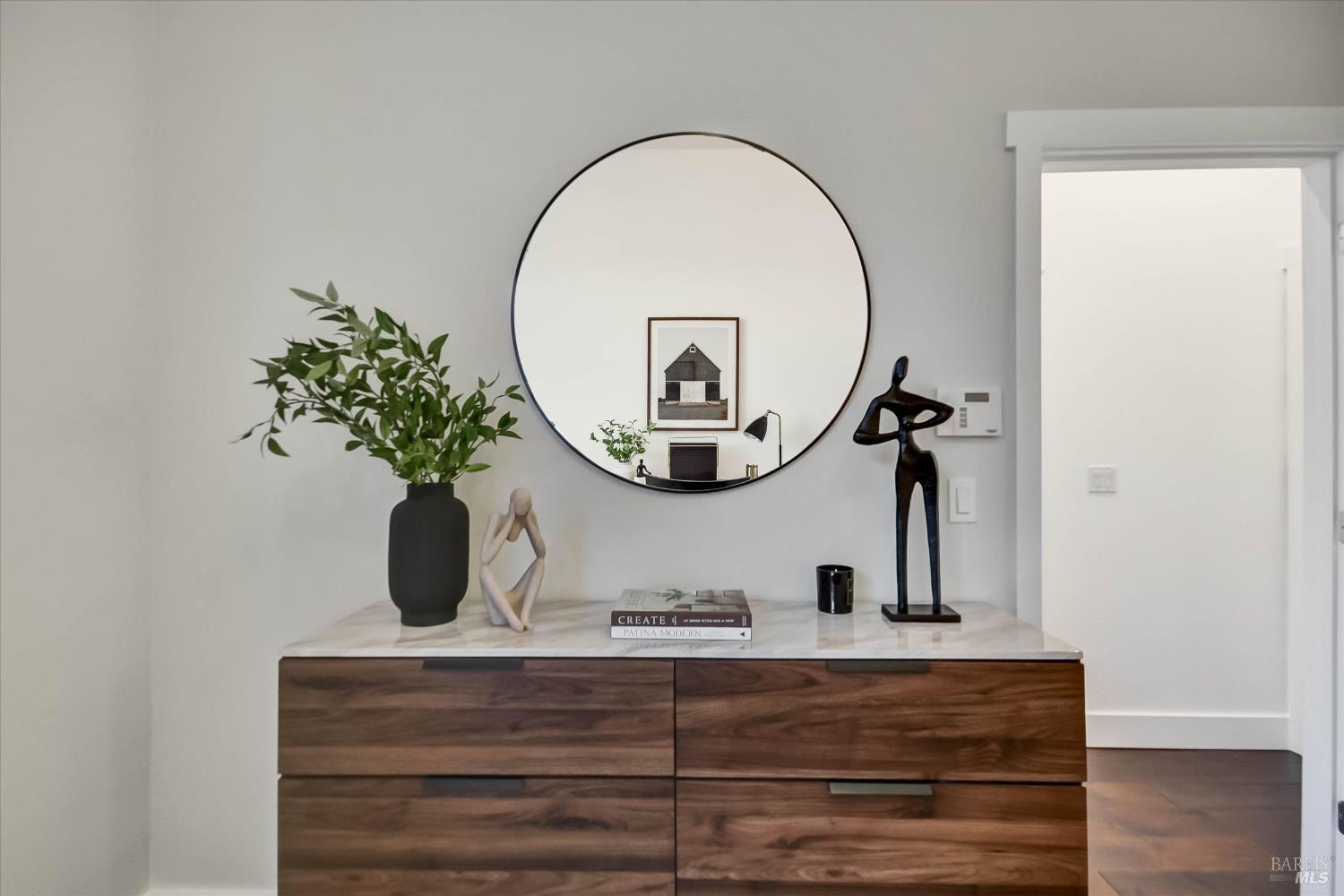 Entryway with a walnut console, round mirror, leafy branches, and sculptural decor.