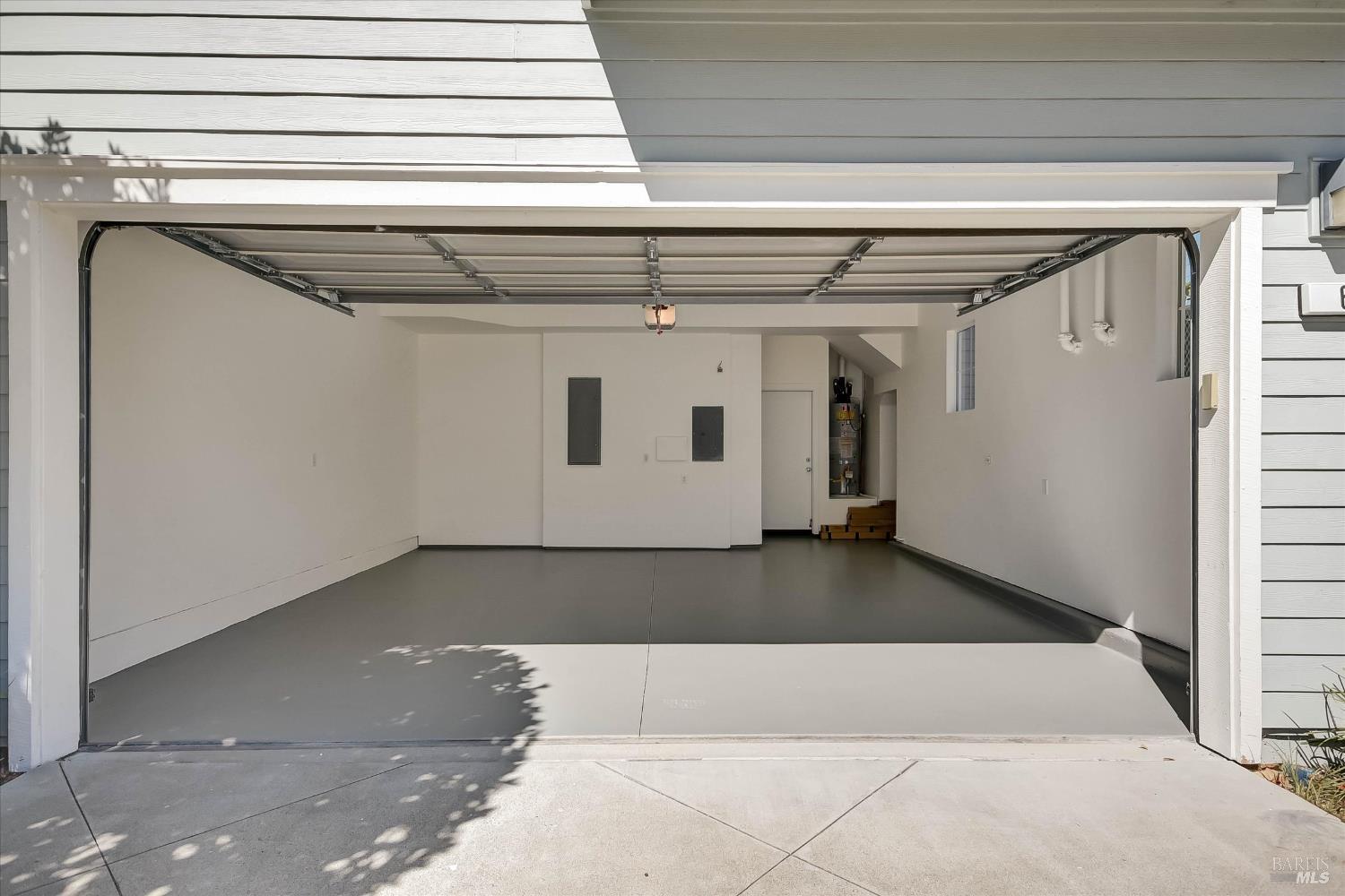 Empty garage with its overhead door open, gray concrete floor, and utility panels at the back.