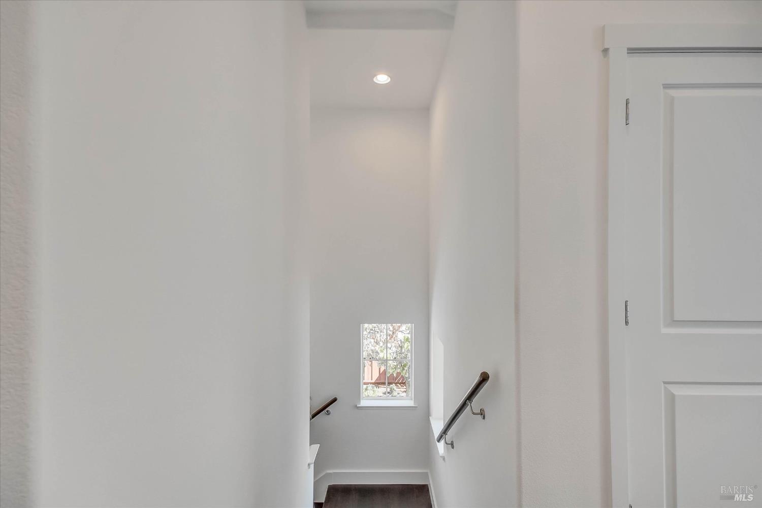 White stairwell with dark steps, metal handrails, and a small window at the landing.