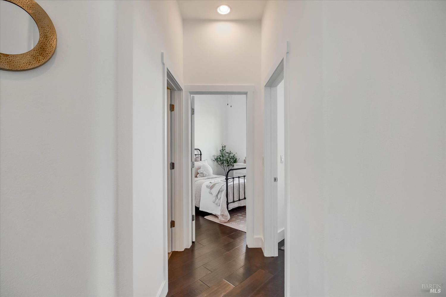 White hallway with dark wood floors opening onto a bedroom with a black metal bed.