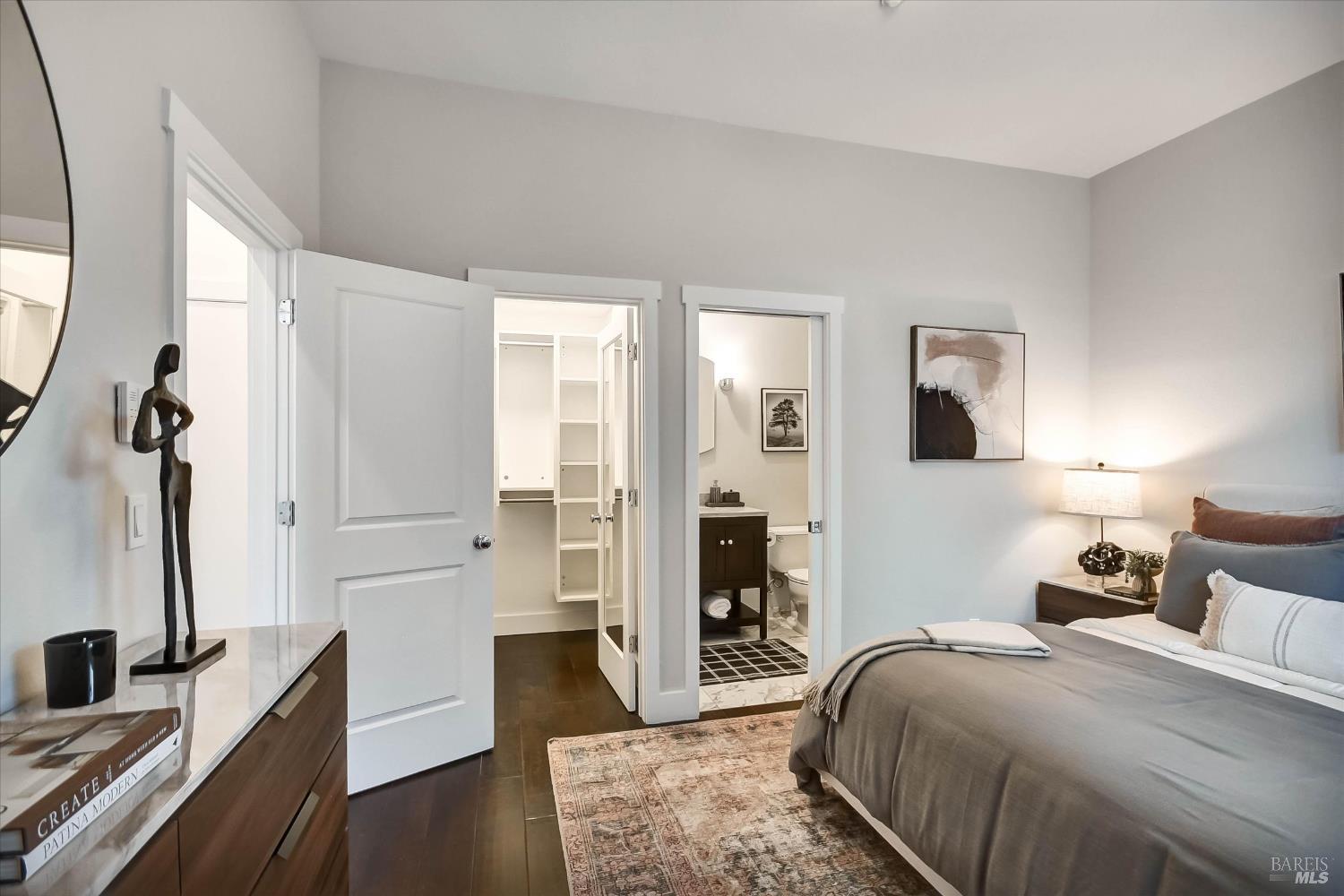 Staged bedroom with gray bedding, a patterned rug, and open doors to a closet and en-suite bathroom.