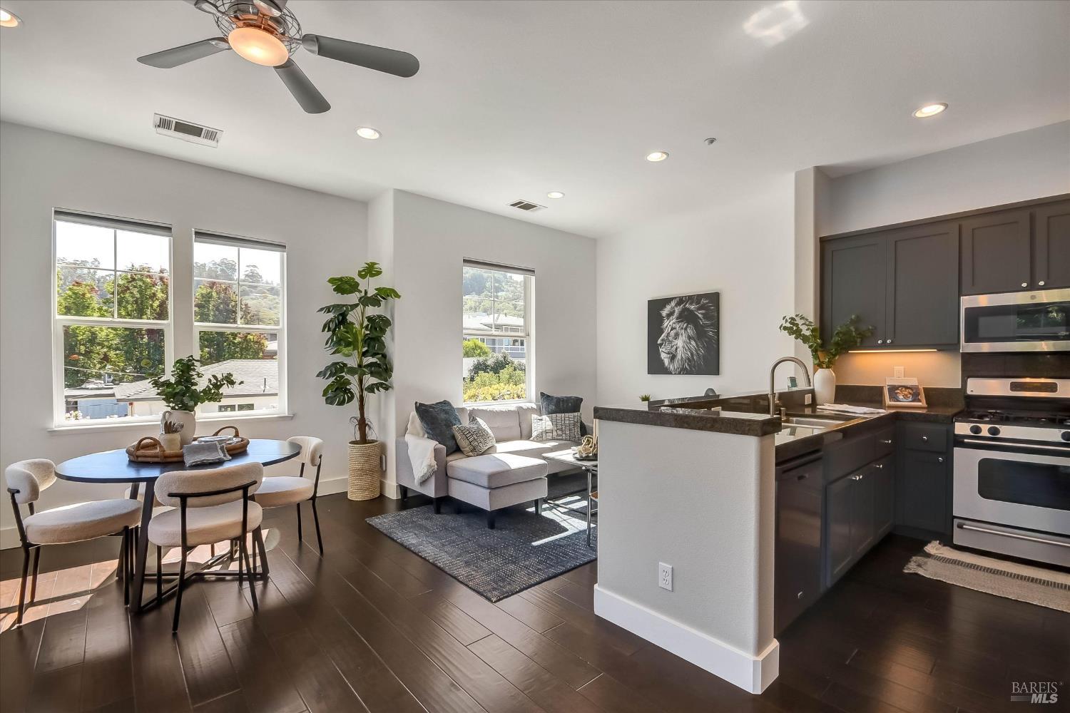 Open-plan kitchen and living area with dark cabinetry, a large island, and windows overlooking greenery.
