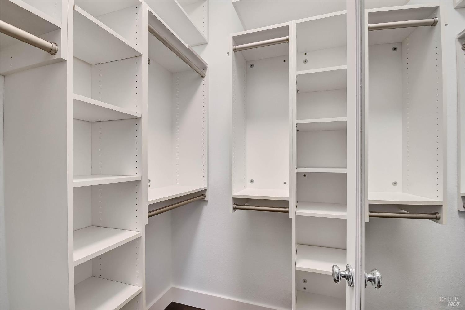 Walk-in closet with empty white built-in shelves and multiple hanging rods.