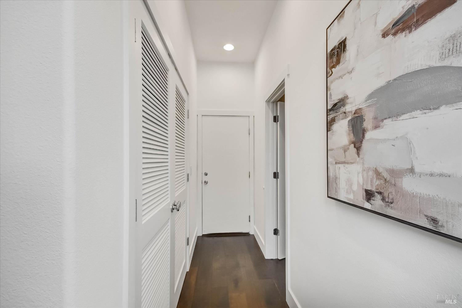 Entry hallway with louvered closet doors, dark wood flooring, and a large abstract painting.