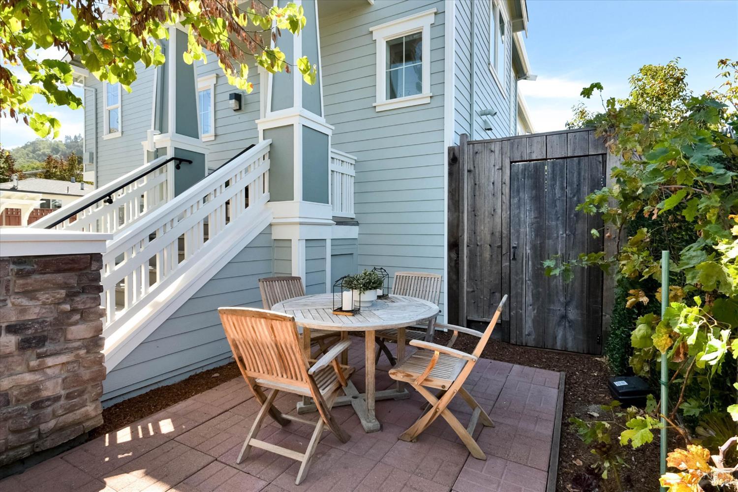 Furnished brick patio beside a blue-gray home, with a dining set and white-railed stairs.