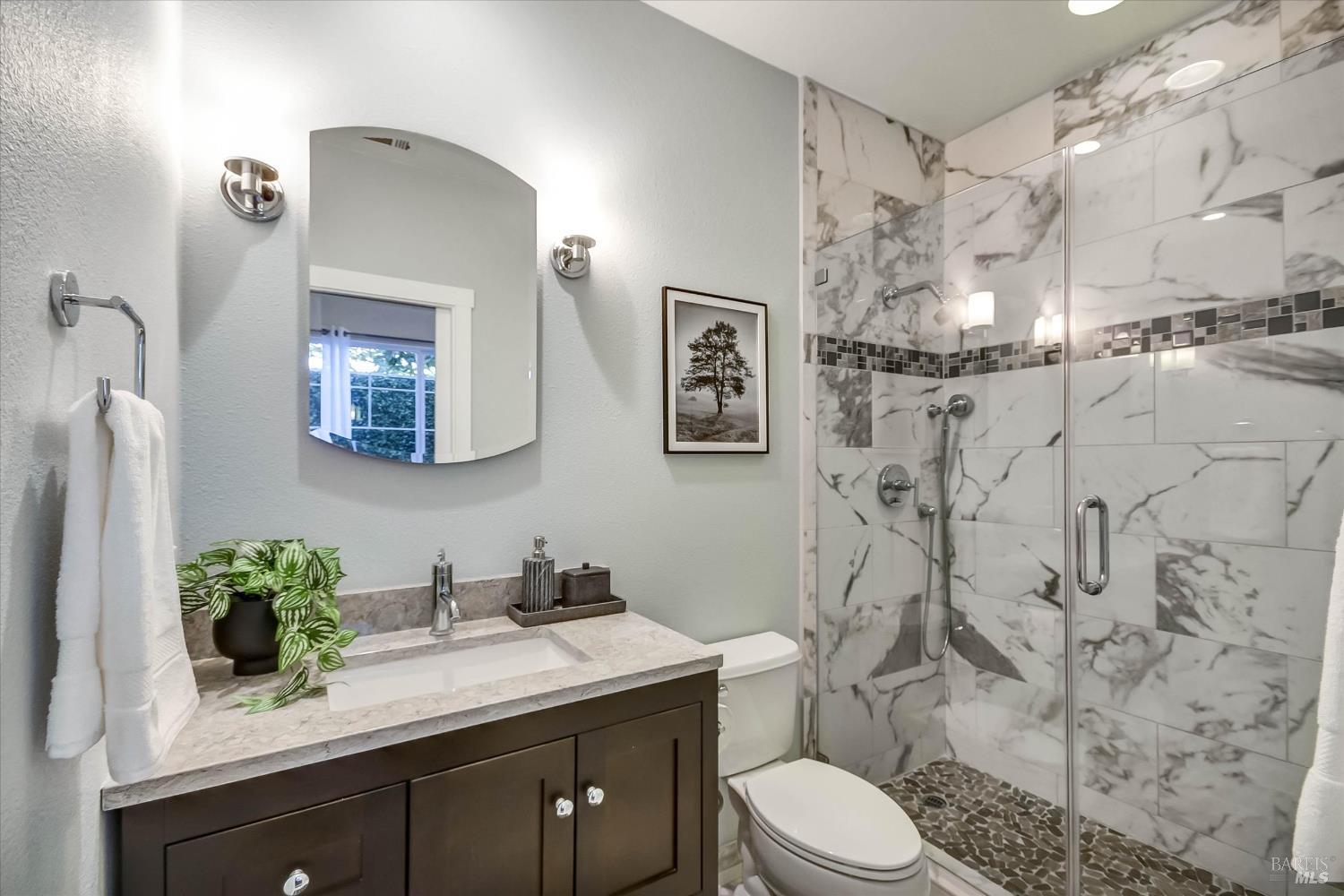 Bathroom with a dark vanity and glass shower clad in gray-veined marble tile.